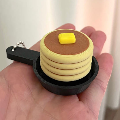 Keychain shaped like a stack of pancakes with a pat of butter on top, held in a hand.