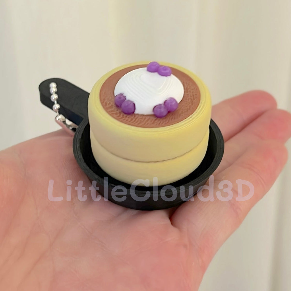 Small cake-shaped keychain held in a hand with a plain background