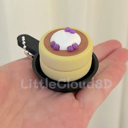 Small cake-shaped keychain held in a hand with a plain background