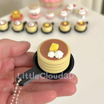 Miniature pancake charm held by a hand with a blurred background of similar charms.